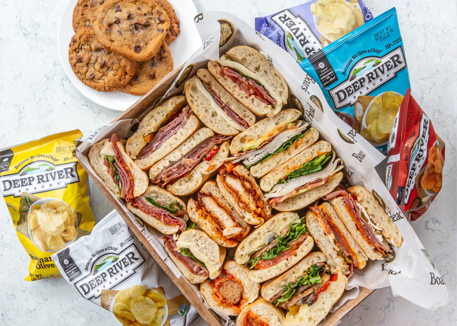 A box of deli sandwiches, a plate of cookies, and chips - the complete deli catering package